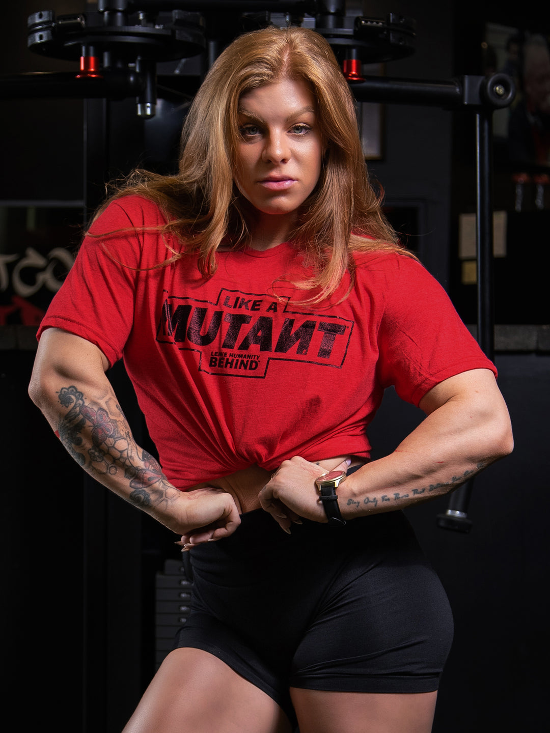 Shelby Guillaume posing at the gym while wearing the red 'MUTANT's Truck Month' t-shirt that features the 'Like a Mutant' phrase and 'Leave Humanity Behind' tagline in black.