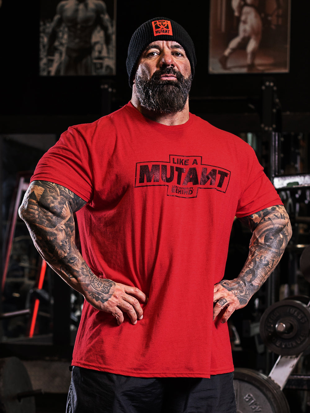 Dusty Hanshaw at the gym, staring at the camera while wearing the red 'MUTANT's Truck Month' t-shirt, which features the 'Like a Mutant' phrase and 'Leave Humanity Behind' tagline in black.