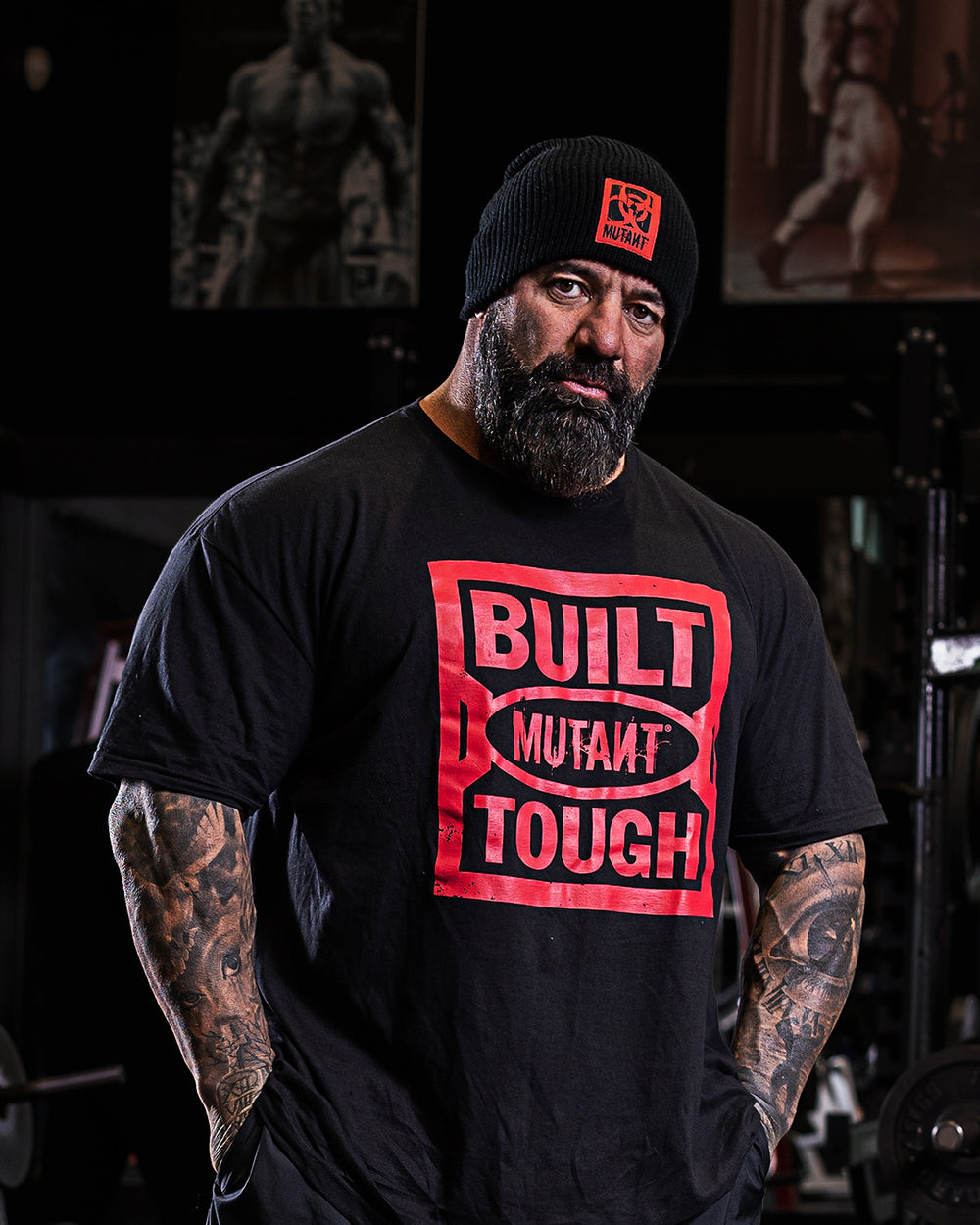 Dusty Hanshaw at the gym, staring at the camera while wearing the black 'MUTANT's Truck Month' t-shirt with the 'Built Mutant Tough' phrase in red letters.
