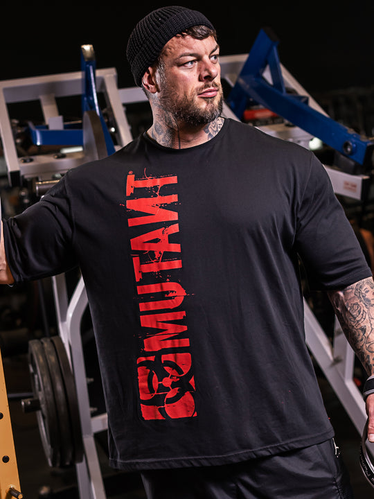 Jamie Christian, Mutant athlete, posing in the gym wearing the Black Free Standing Oversized Gym T-Shirt featuring a vertical Mutant red logo.