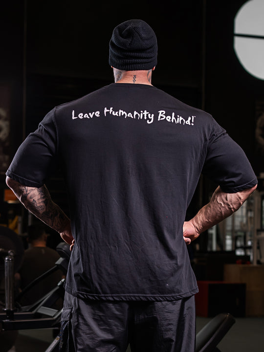  Back view of Jamie Christian, Mutant athlete, posing in the gym wearing the Black Free Standing Oversized Gym T-Shirt featuring Mutant's tagline 'Leave Humanity Behind' in white.