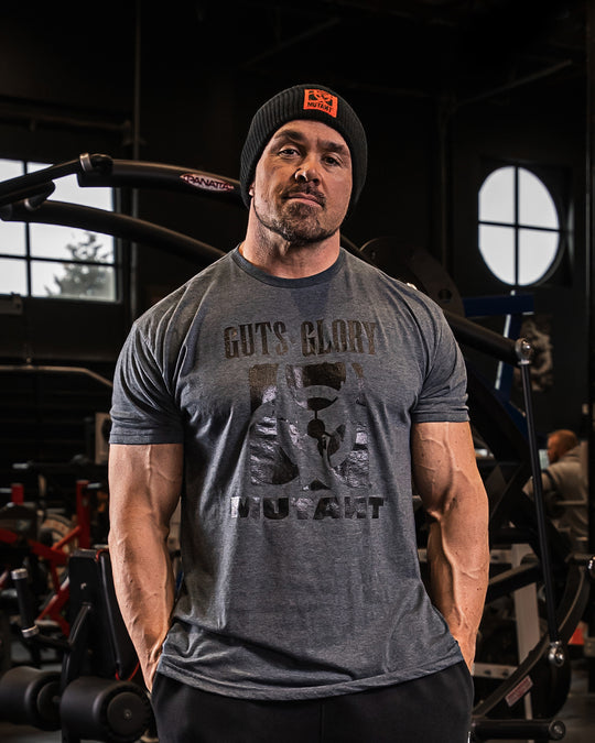 Big Ron Partlow at the gym wearing the grey 'MUTANT's Truck Month' t-shirt featuring the 'Guts, Glory, Mutant' phrase and the MUTANT logo in black.
