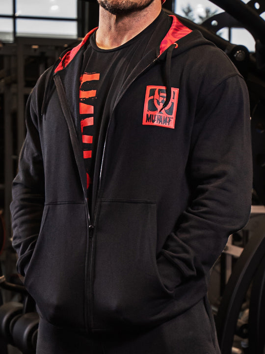 Close-up photo of a Mutant athlete wearing the Black Mutant Patched Zip-Up Gym Hoodie. The image focuses on the red and black Mutant logo patch on the left chest.