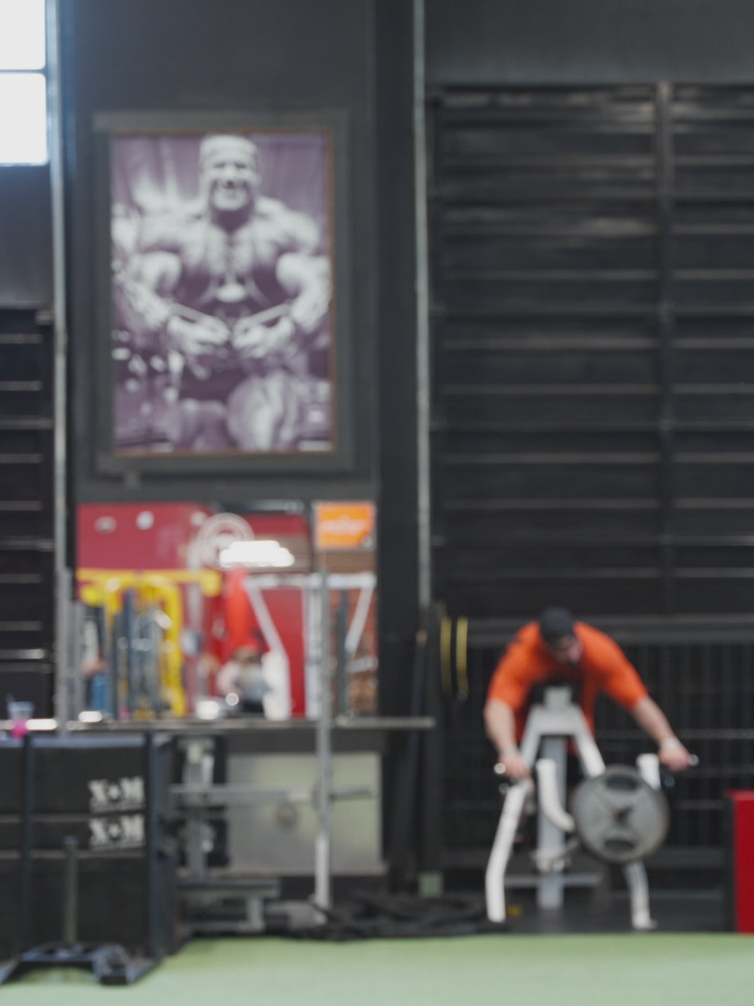 A video featuring Big Ron Partlow at the gym, posing to showcase both the front and back of the black 'MUTANT's Truck Month' t-shirt which has the 'Built Mutant Tough' slogan in red letters.